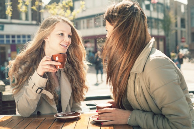Two young girl-friends talking and drinking coffee in cafe, outdoors